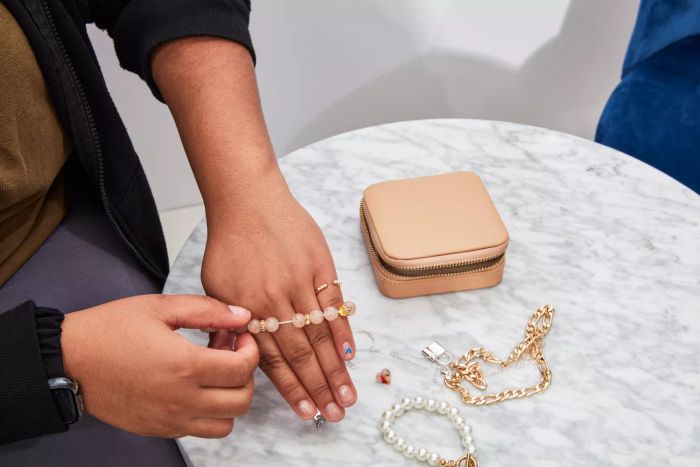 A person removing a bracelet from near the Mejuri Travel Case placed on a marble table top