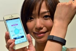 A woman shows off a smart bracelet while displaying the companion app.