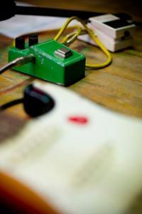 A guitar pedal and guitar are placed in the foreground, highlighting the essential connection between the instrument and the effects used to shape its sound.