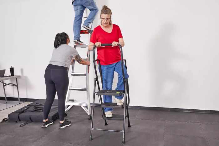 A person uses the Delxo Three-Step Folding Step Stool Ladder while two others climb different ladders nearby.