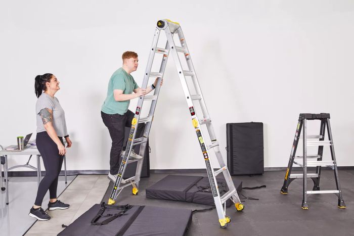 A person climbing the Gorilla Ladders 19-Foot Reach MPXT Multi-Position Ladder with Project Top, while another individual watches nearby