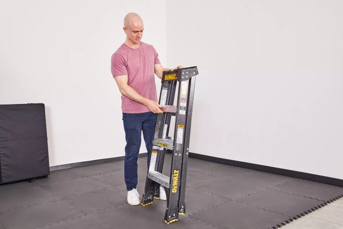 A person is seen holding a folded DeWalt 4-Foot Fiberglass Step Ladder.
