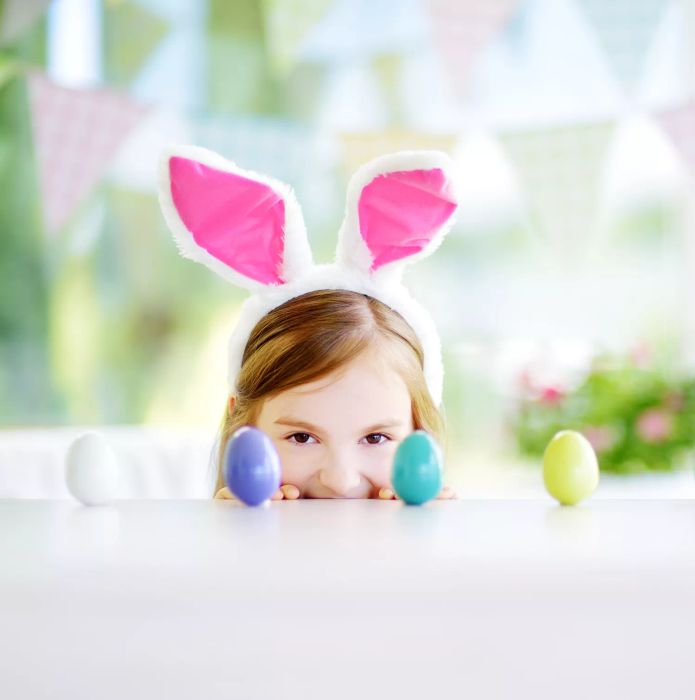 A child wearing bunny ears, gazing at a table filled with a colorful assortment of Easter eggs.