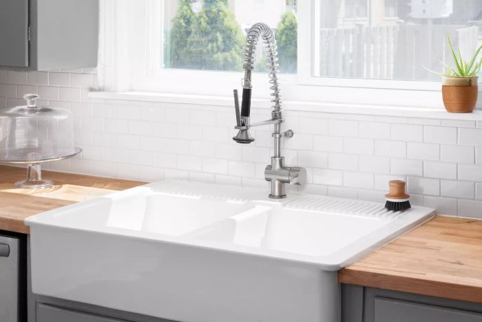 A kitchen sink detail featuring butcher block countertops, white subway tile backsplash, grey cabinets, and a classic farmhouse sink.
