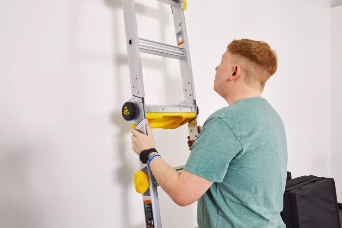 A person holding a Gorilla Ladders 19-Foot Reach MPXT Multi-Position Ladder with Project Top against a wall 