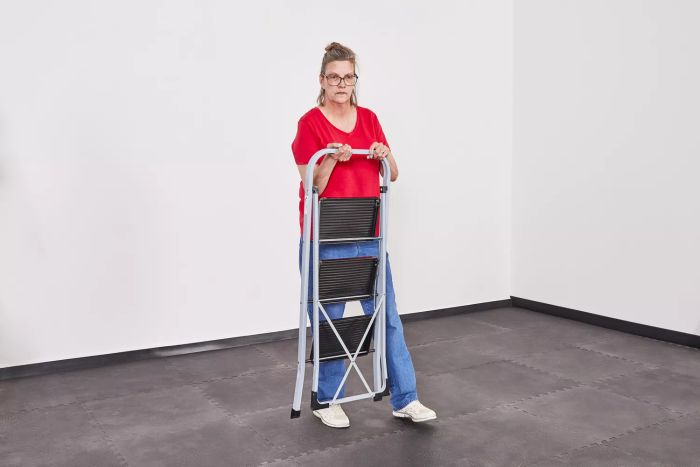 A person holding a compact Delxo Three-Step Folding Step Stool Ladder