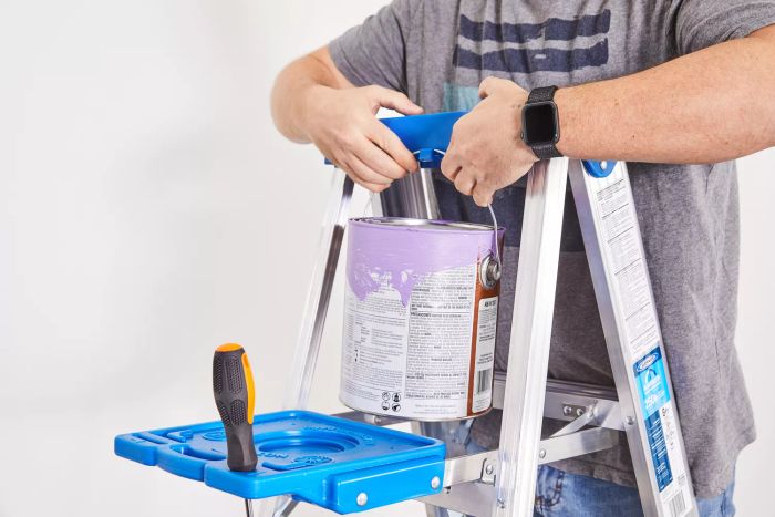 A person suspending a paint bucket on a hook at the top of the Werner Aluminum Stepladder