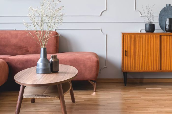 Dried flowers in a chic dark vase placed on a wooden coffee table in front of a warm, ginger-hued corner sofa