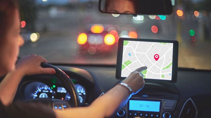 A woman is seen from behind, driving her car and interacting with the navigation system screen.
