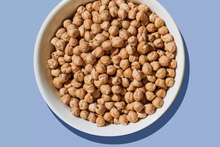 A white bowl filled with chickpeas, set against a purple backdrop