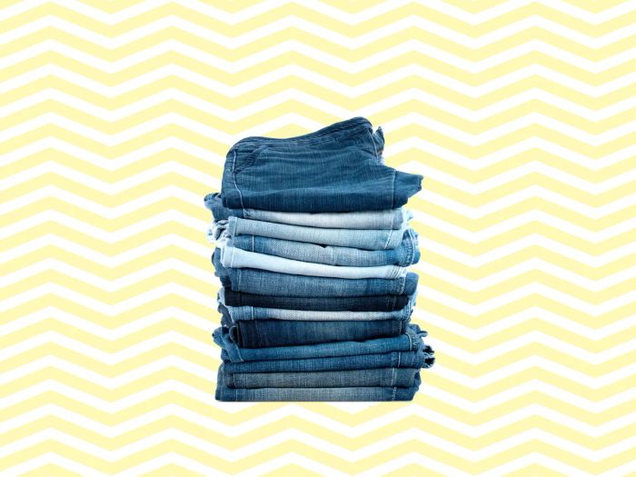 A stack of thirteen neatly folded jeans in various shades set against a vibrant yellow and white chevron background