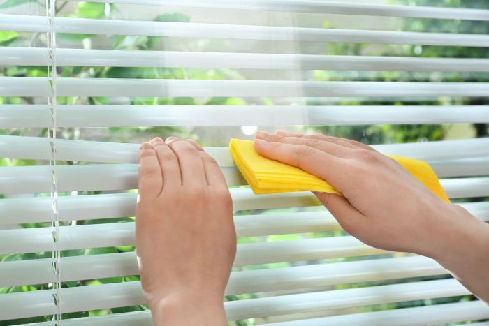 Hands holding a rag to wipe down white blinds