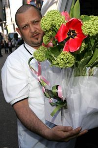 A delivery person holding a bouquet of flowers on a sidewalk.
