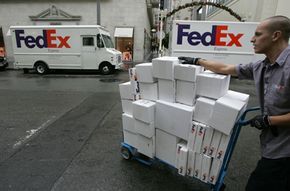 A Fed Ex worker pushes a dolly loaded with packages past two Fed Ex trucks.
