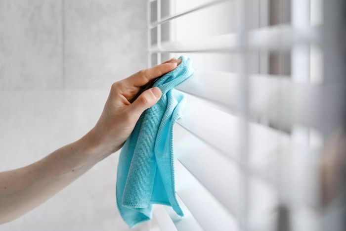 Close-up shot of a hand wiping white blinds with a blue microfiber cloth