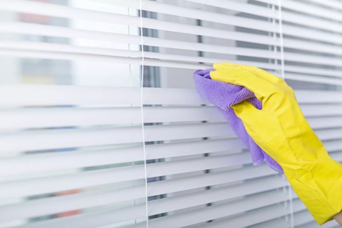 A person using a purple rag to clean blinds