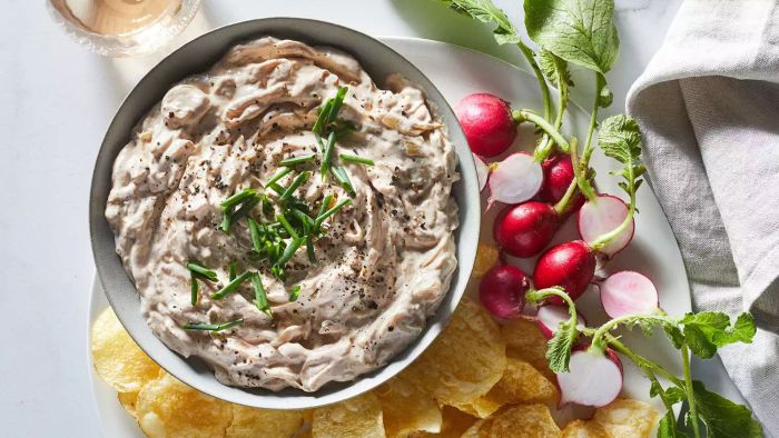 A top-down view of a bowl filled with Deeply Caramelized Onion Dip, served with chips and radishes