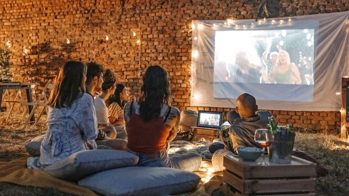 A picture of friends enjoying a movie night outdoors in the backyard.