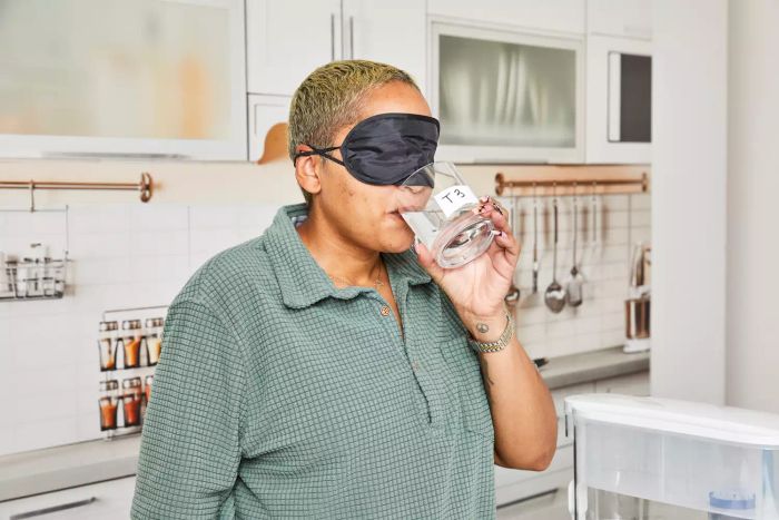 A person sips water from the Pur Plus 30-Cup Dispenser while blindfolded