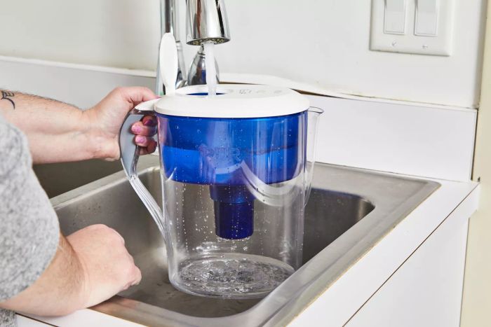 A person fills the Pur Classic 11-Cup Water Filter Pitcher with water from the faucet
