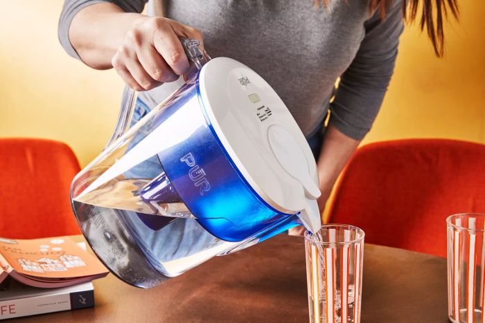 A person pours water from the Pur Classic 11-Cup Water Filter Pitcher into a glass