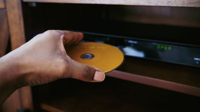 A close-up shot of a woman placing a disc into a DVD player.