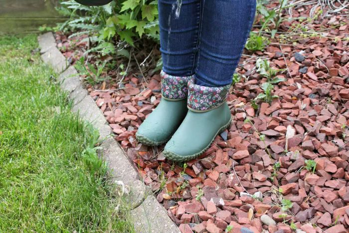 A woman wearing The Original Muck Boot Company Women's Muckster II Mid Boot walking on gravel outdoors.