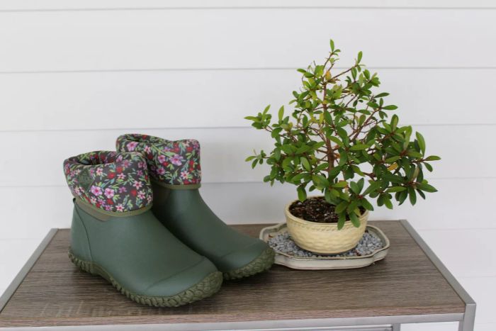 The Original Muck Boot Company Women's Muckster II Mid Boot shown on a wooden table beside a small plant.