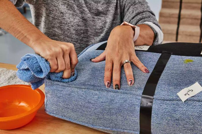 Hands rubbing a cushion with a rag and OxiClean Total Interior Carpet & Upholstery Cleaner.