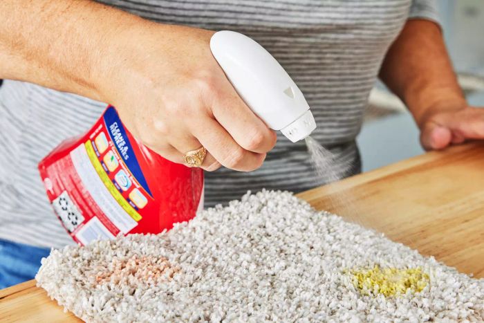 A hand spraying upholstery cleaner onto a carpet sample.