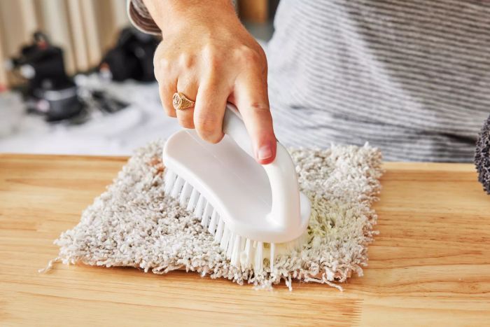 A hand scrubbing a piece of carpet with a brush using Resolve Multi-Fabric Cleaner & Upholstery Stain Remover.