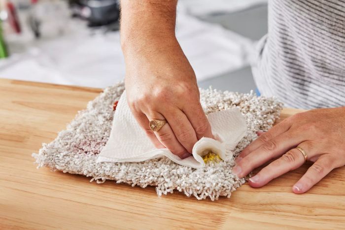 A person scrubbing a stain on a piece of carpet using a napkin.