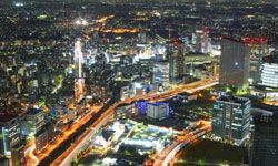 Photograph of a city skyline under the night sky, with lights gleaming across the buildings and streets.