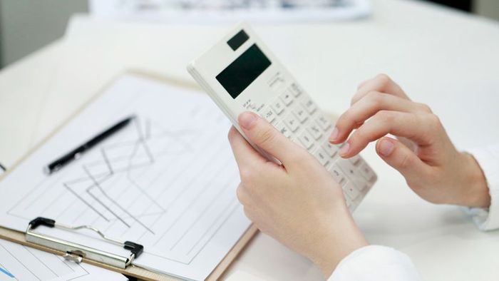 A woman working with a white calculator on her desk.