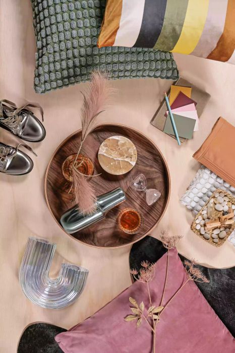 Aerial view of decorative items, dark wooden tray, pillows, and a fluted glass vase