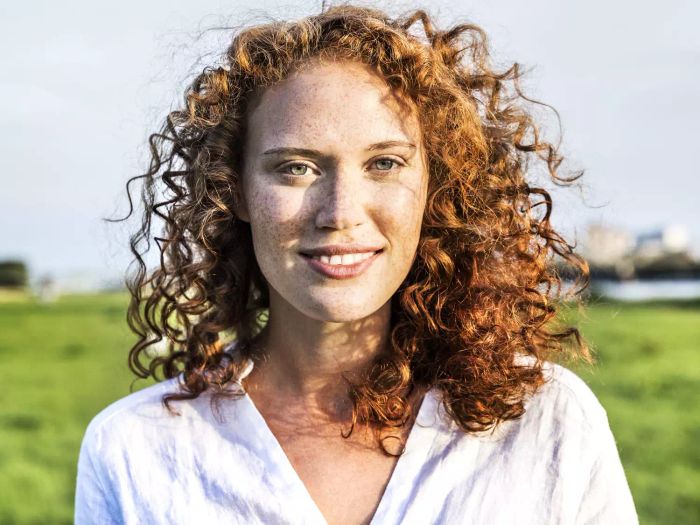 A portrait of a freckled young woman with curly red hair.