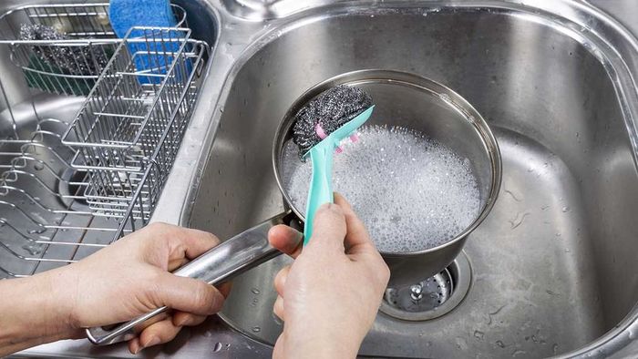 Person scrubbing an aluminum pot using cream of tartar and soap.