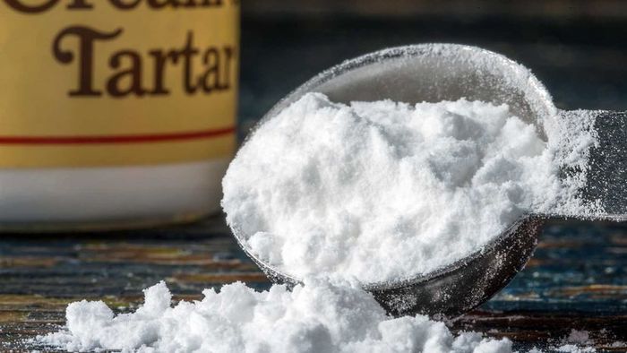 A spoonful of cream of tartar powder with the jar visible in the background.