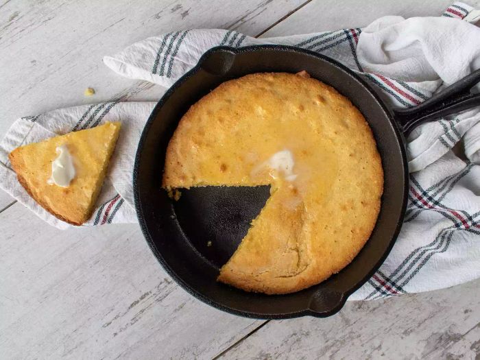 Overhead view of cornbread in an iron skillet with one piece removed