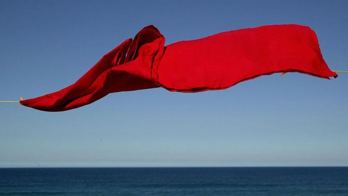 A red sheet hanging on a clothesline by the ocean.