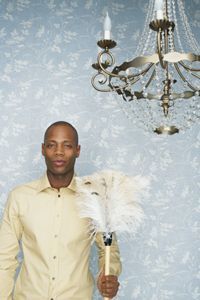 A man holding a feather duster, standing under a chandelier.
