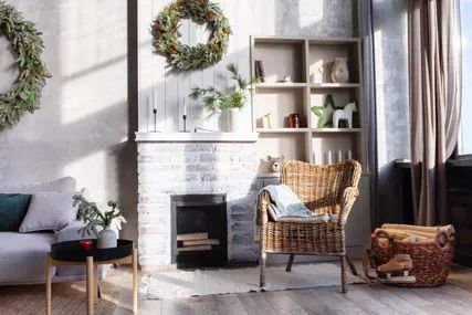 A tidy, serene home with a whitewashed fireplace, a woven rattan side chair, and evergreen wreaths