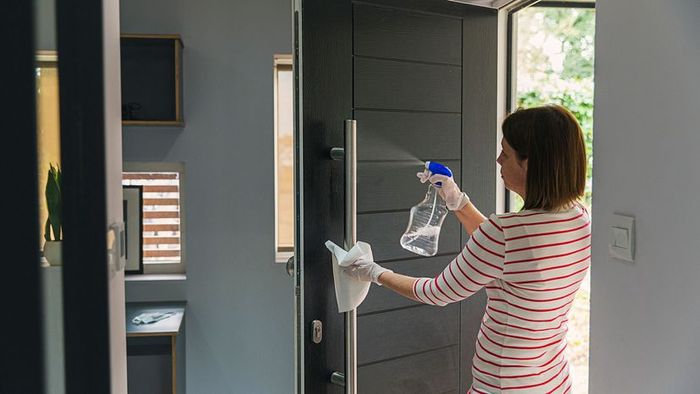 A woman applying sanitizer or disinfectant on a door handle.