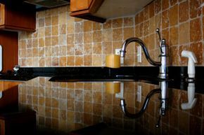 A sleek, black kitchen countertop reflecting a shiny silver faucet.