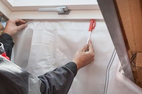 A close-up view of someone installing a vapor barrier around the skylight in an attic.