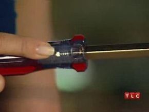 A person gripping a dark screwdriver with red stripes on the handle.