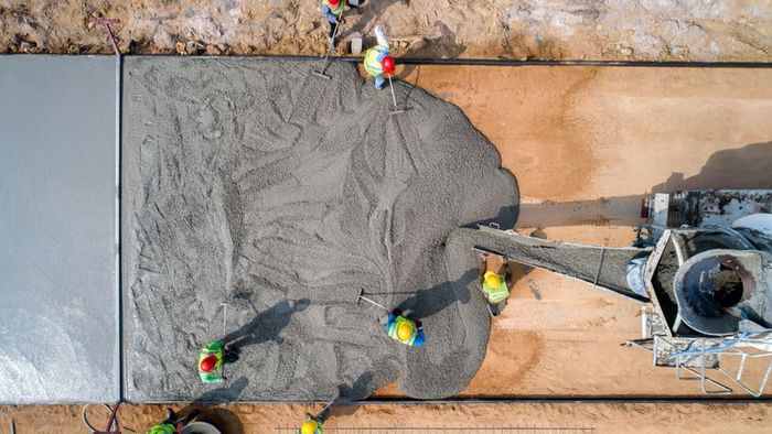 A construction worker is seen pouring fresh, wet concrete at a busy construction site.