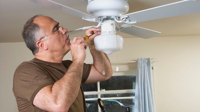 A person repairing a ceiling fan with a screwdriver.
