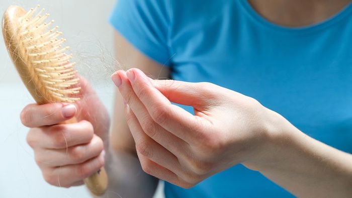 A woman removes hair from a wooden hairbrush.