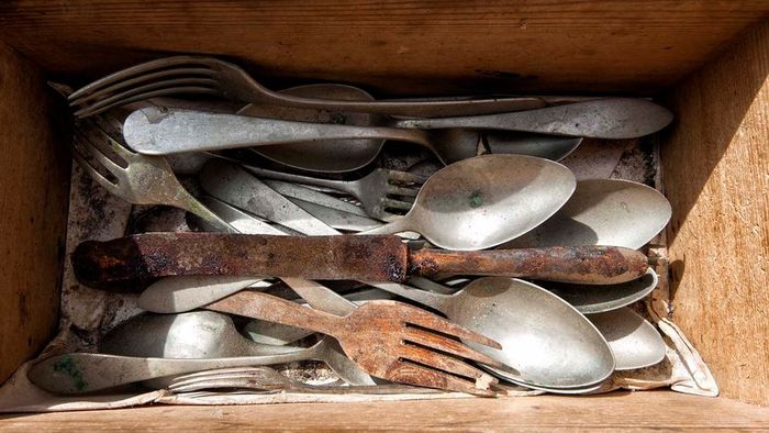 A collection of old, rust-covered utensils stored in a wooden box.